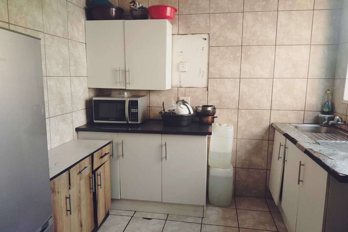A functional kitchen featuring tiled walls, built-in cabinetry, and a stainless steel sink, currently showing signs of wear and dated finishes.
