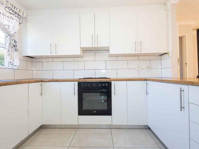 A clean, modern kitchen featuring white cabinetry, wooden countertops, a subway tile backsplash, and a built-in oven with a hob.