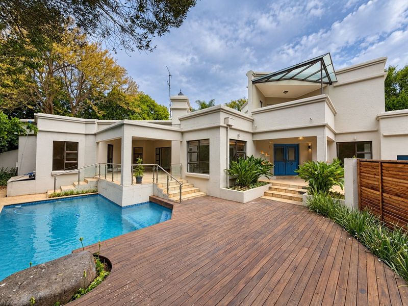 Rear exterior view featuring a swimming pool, expansive timber decking, covered patio area, and a modern multi-level architectural design with glass accents.