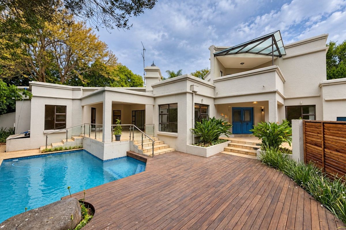 Rear exterior view featuring a swimming pool, expansive timber decking, covered patio area, and a modern multi-level architectural design with glass accents.