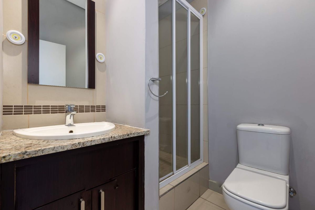 A compact bathroom featuring a granite-topped vanity, a framed mirror, a glass-enclosed shower, and a modern toilet.