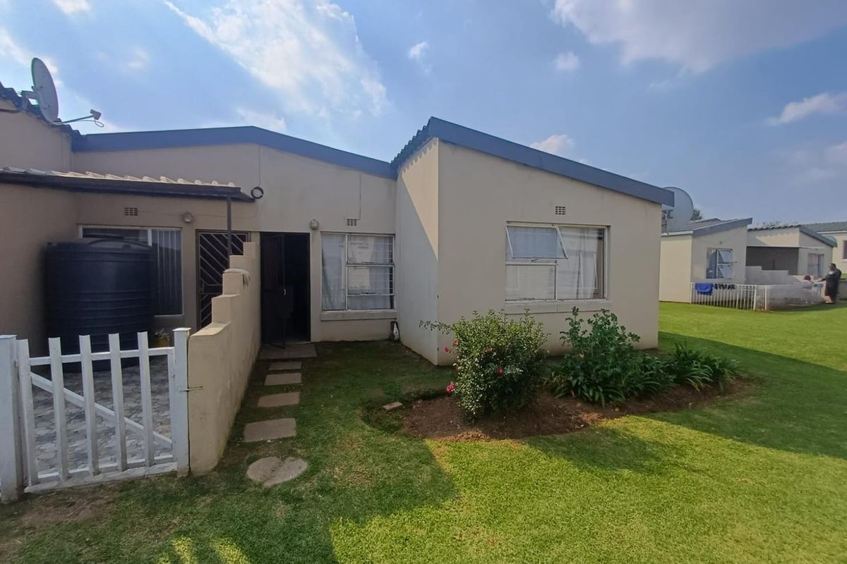 Rear view of the townhouse featuring a small garden, paved path, security gate, and a water storage tank.