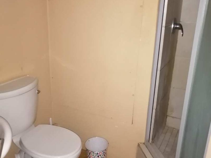 A compact bathroom featuring a standard toilet and a glass-enclosed shower stall, requiring cosmetic updates to the flooring and wall finishes.