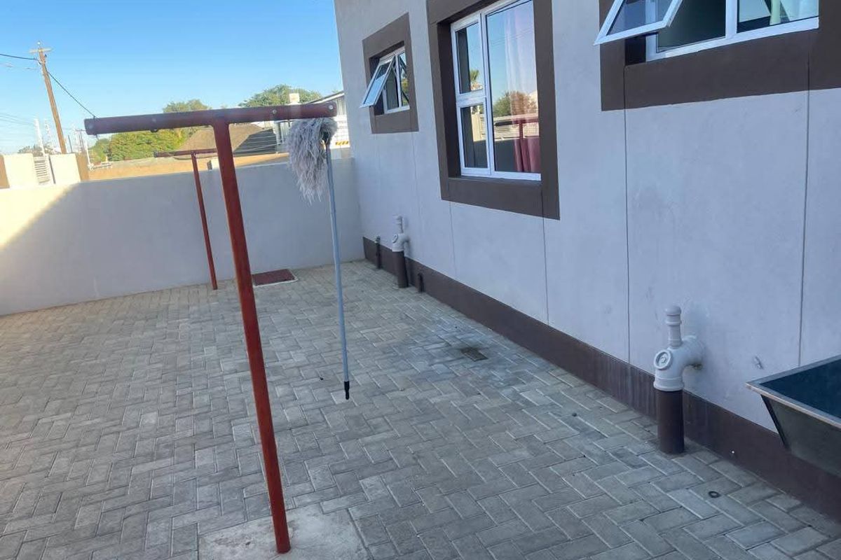 A paved outdoor utility area featuring a fixed washing line, external plumbing connections, and a wall-mounted basin against the building exterior.