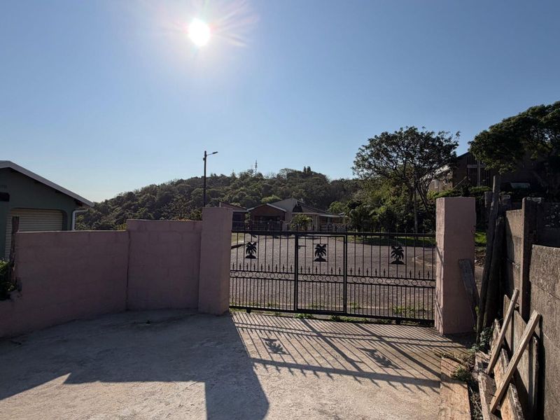 Front entrance view of the property featuring a metal security gate, concrete boundary walls, and a paved driveway area.