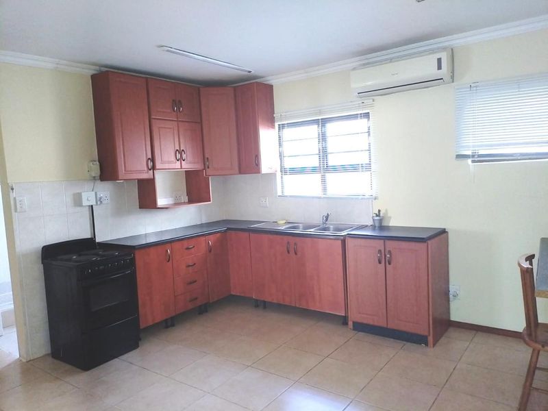 A functional kitchen featuring wood-tone cabinetry, tiled flooring, a double bowl sink, and a wall-mounted air conditioning unit.