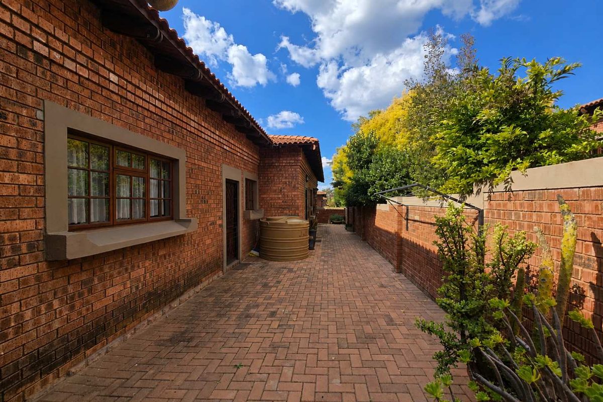 A side exterior walkway featuring red face-brick walls, paved flooring, and a water storage tank, providing a functional outdoor utility space.