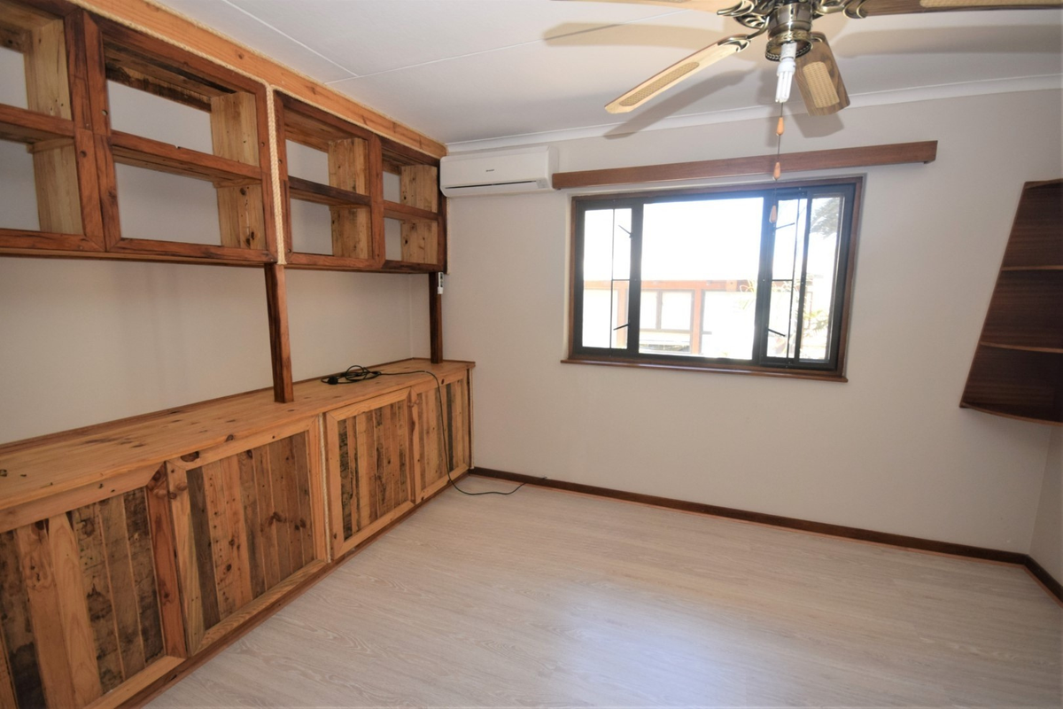 A bedroom featuring built-in timber shelving and cabinetry, light-toned laminate flooring, a ceiling fan, and a wall-mounted air conditioning unit.