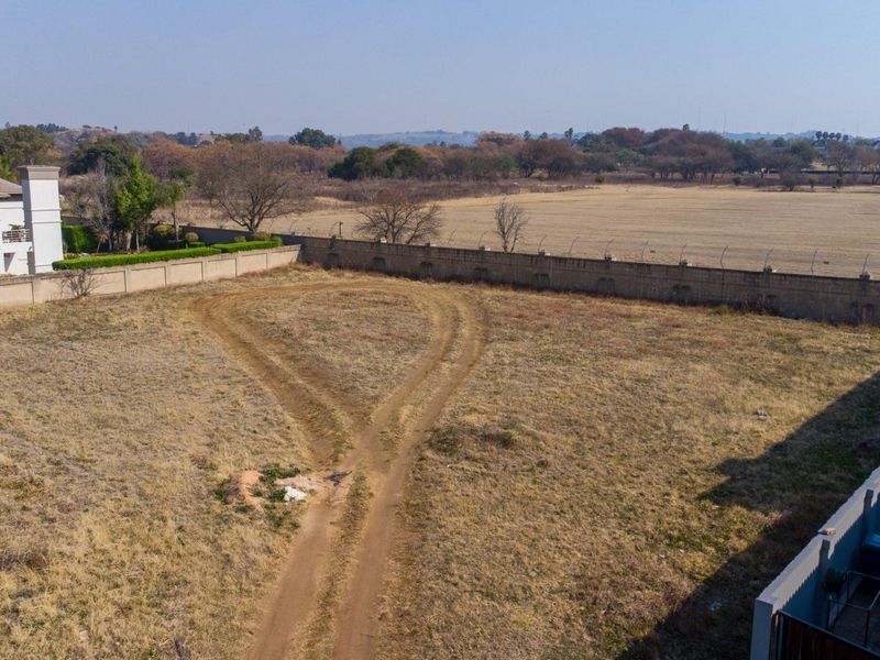 An aerial view of a vacant residential plot featuring a perimeter wall and security fencing, ready for development.