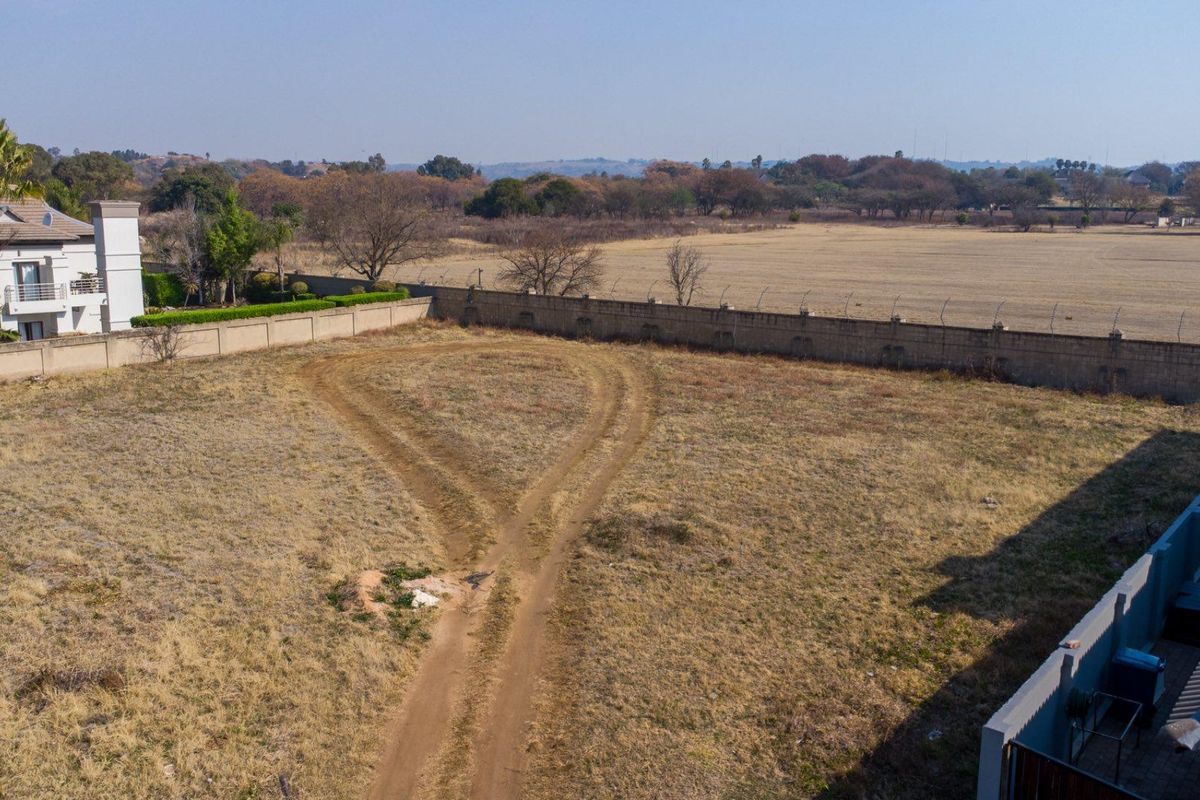 An aerial view of a vacant residential plot featuring a perimeter wall and security fencing, ready for development.