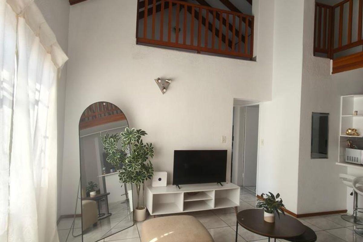 Spacious living area featuring high vaulted ceilings with exposed timber beams, a mezzanine level with timber balustrade, and bright tiled flooring.