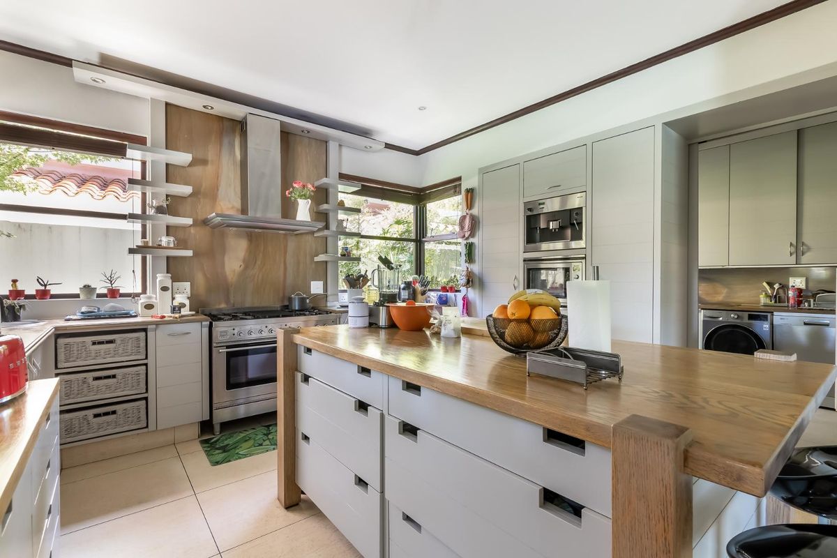 Modern kitchen featuring a large central island with a wooden countertop, stainless steel gas range, built-in oven, and integrated cabinetry.