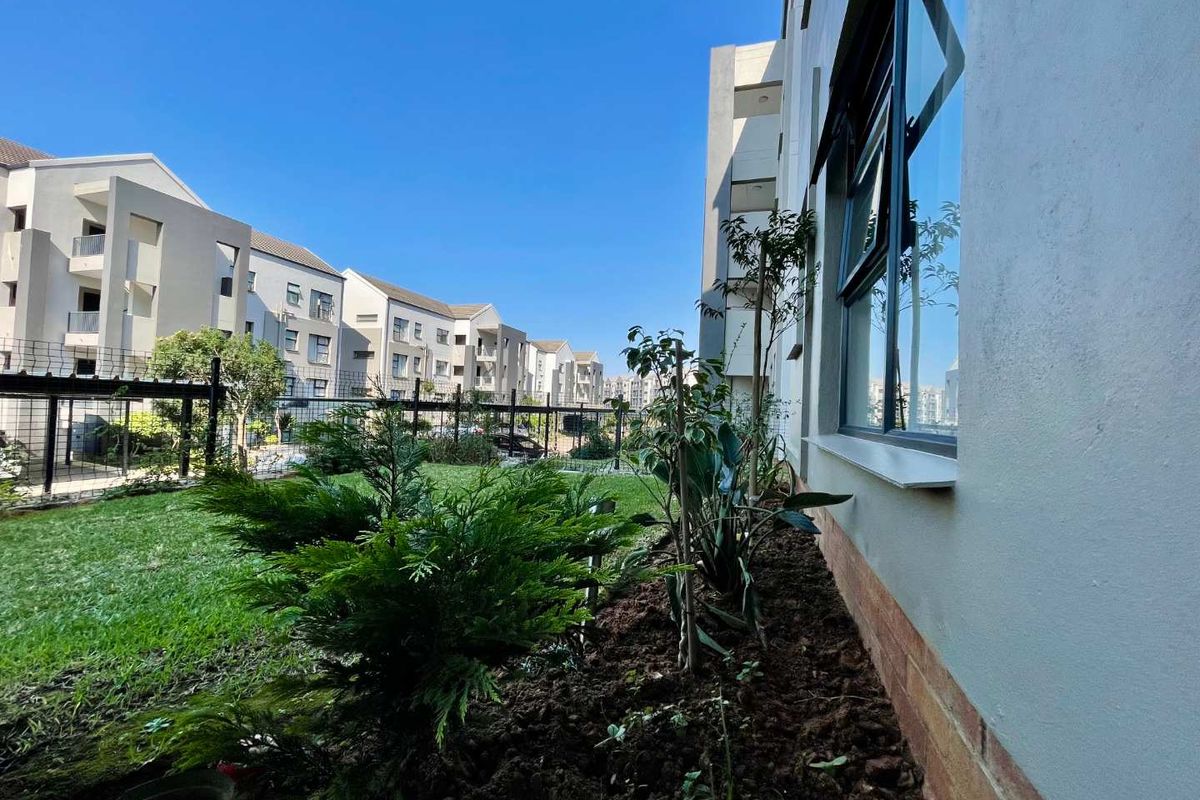 A view of the rear garden area of the apartment complex, featuring landscaped greenery and secure perimeter fencing.