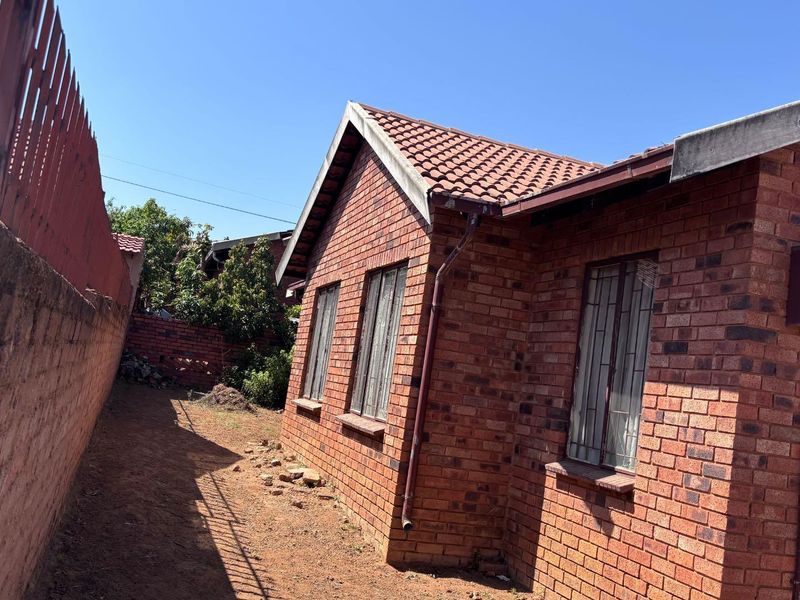 A view of the rear exterior of the face brick house, featuring a tiled roof, security bars on windows, and a surrounding boundary wall.