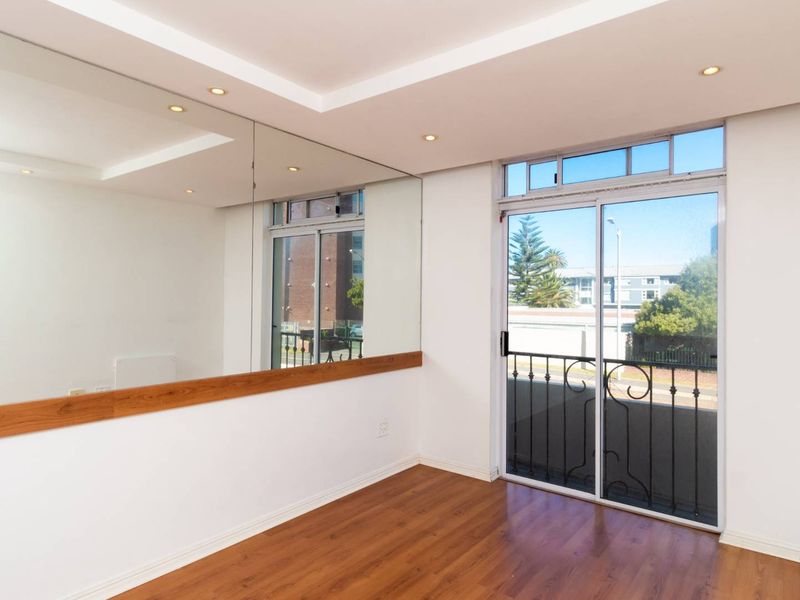 Bright and spacious living area featuring laminate flooring, recessed ceiling lights, a large wall mirror, and a sliding glass door leading to a balcony.