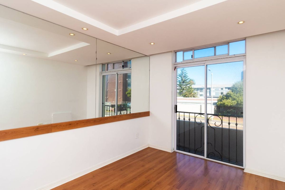 Bright and spacious living area featuring laminate flooring, recessed ceiling lights, a large wall mirror, and a sliding glass door leading to a balcony.