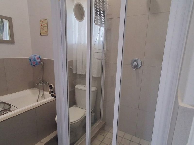 A functional bathroom featuring a built-in bathtub, a separate shower enclosure with a glass door, and a standard toilet with neutral wall tiling.