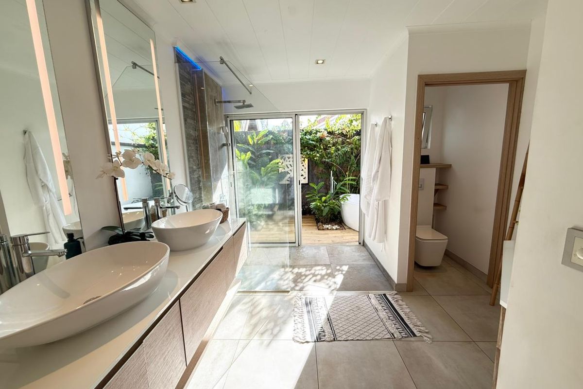 Modern bathroom featuring dual vessel sinks, floating vanity, walk-in shower, and a separate toilet area with direct access to a private outdoor garden space.