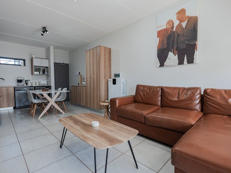 An open-plan living and kitchen area featuring modern tiled flooring, neutral walls, and functional built-in cabinetry with a contemporary layout.