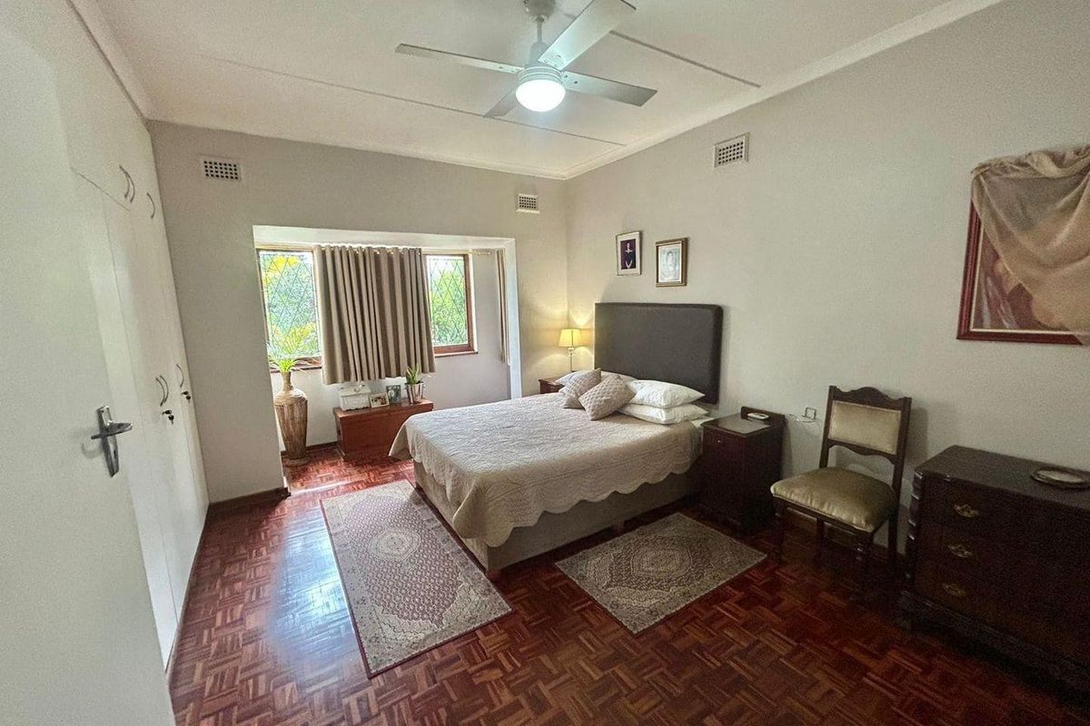 A spacious bedroom featuring classic parquet flooring, built-in cupboards, and a ceiling fan, offering a comfortable and well-lit living space.