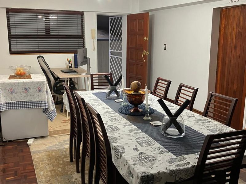 Dining room featuring parquet flooring, timber door, and security gate, providing a functional space with natural light through venetian blinds.