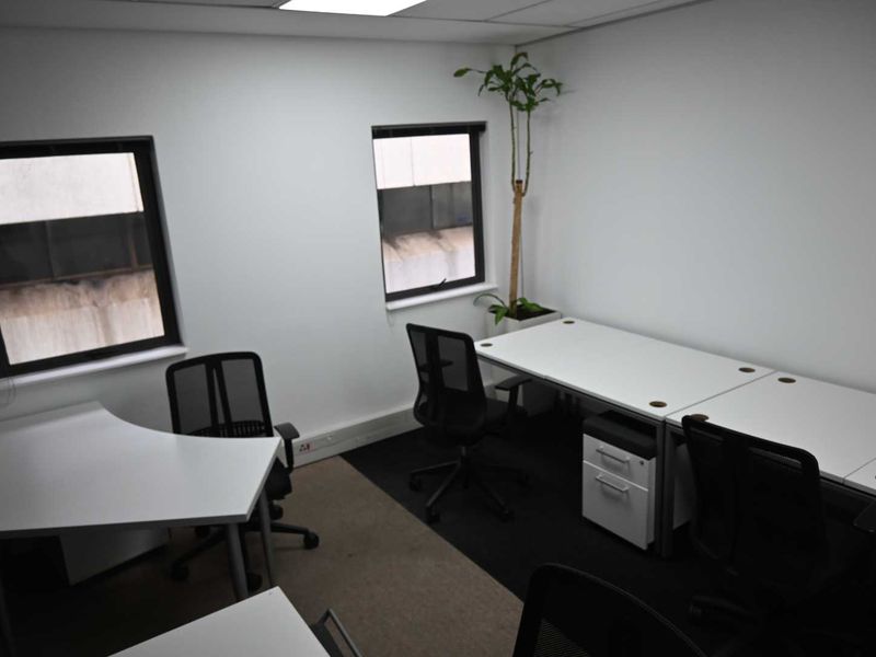 A functional office space featuring neutral walls, recessed ceiling lighting, and dual windows providing natural light.