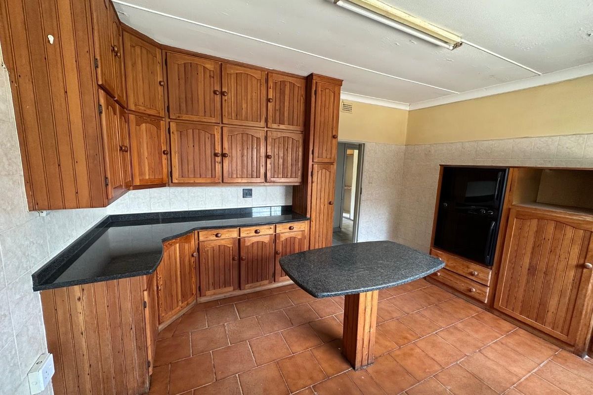 A dated kitchen featuring traditional timber cabinetry, dark laminate countertops, a central island, and terracotta-style floor tiles.