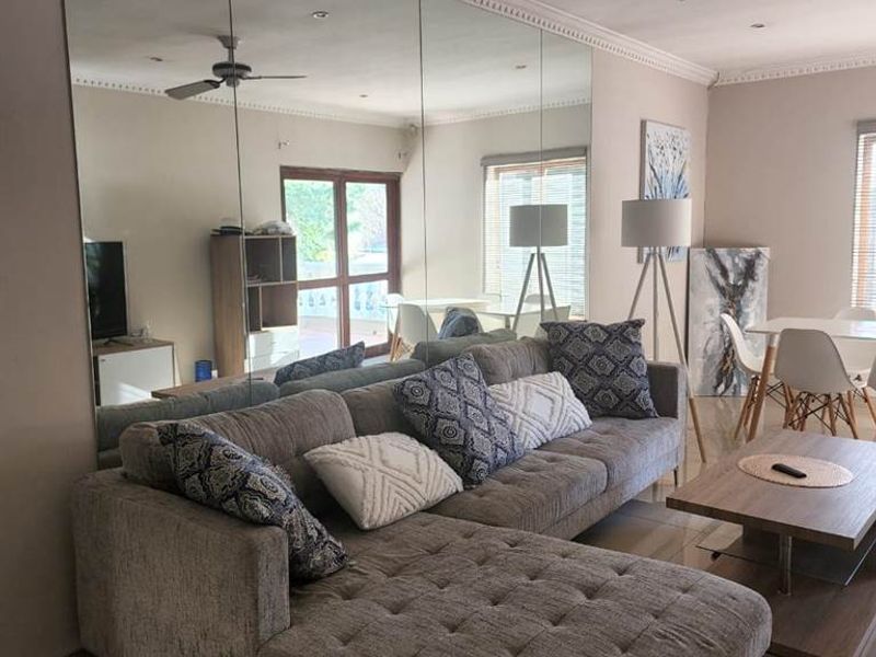 Spacious living area featuring large wall-to-wall mirrors, tiled flooring, and a ceiling fan, creating an open and bright atmosphere.