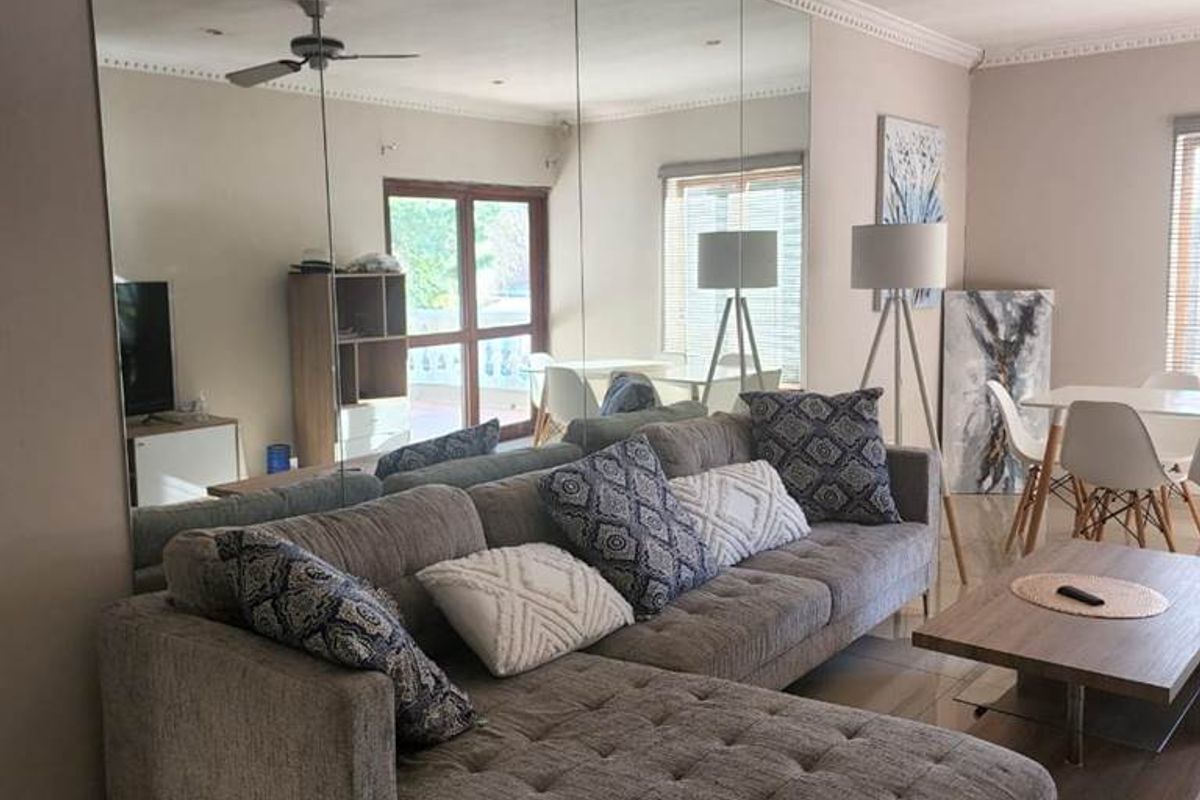 Spacious living area featuring large wall-to-wall mirrors, tiled flooring, and a ceiling fan, creating an open and bright atmosphere.