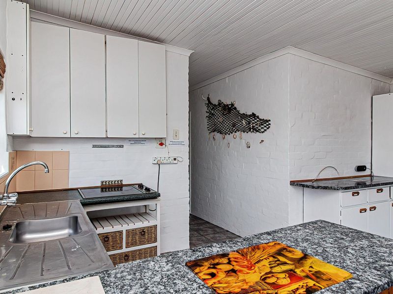 A functional kitchen featuring granite countertops, built-in cabinetry, a stainless steel sink, and an electric hob, with painted brick walls and a tongue-and-groove ceiling.