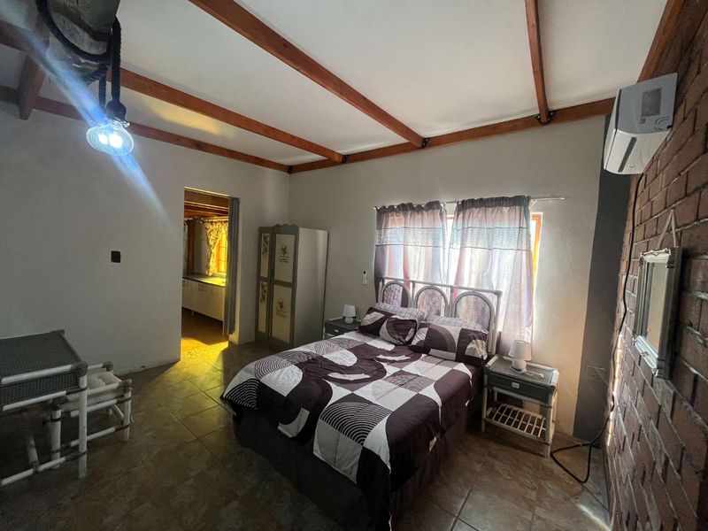 A bedroom featuring exposed timber ceiling beams, an exposed brick feature wall, tiled flooring, and a wall-mounted air conditioning unit.