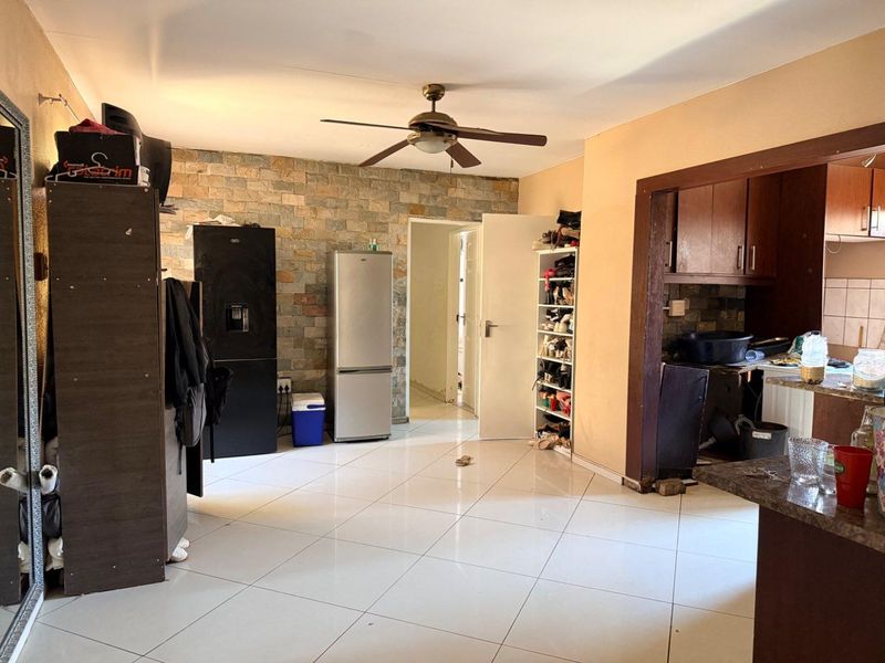Open plan living area featuring tiled floors, a stone accent wall, and a ceiling fan, adjacent to a functional kitchen space.
