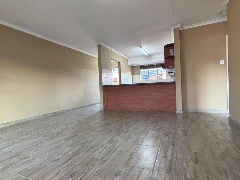 Spacious open-plan living area featuring wood-look tile flooring and a functional kitchen with a breakfast bar and built-in cabinetry.