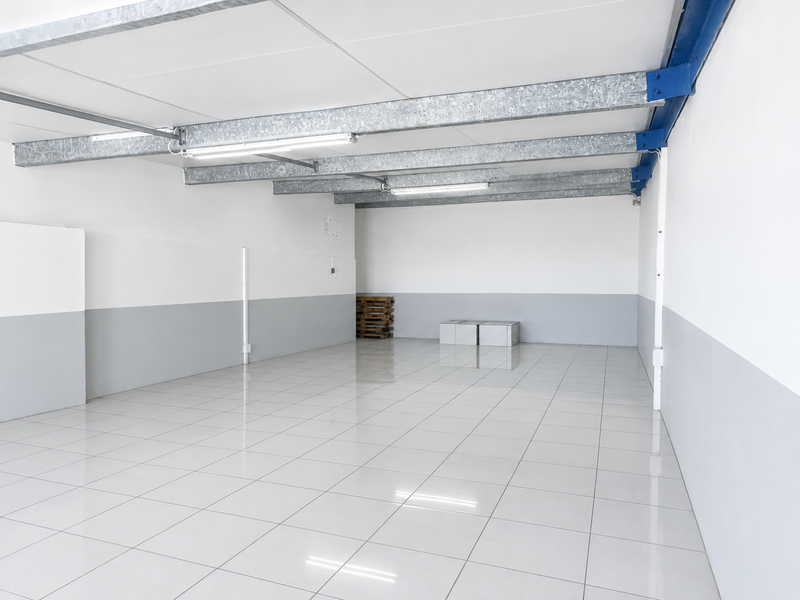 A clean, open-plan utility or storage space featuring polished ceramic tile flooring, exposed industrial steel beams, and bright fluorescent lighting.