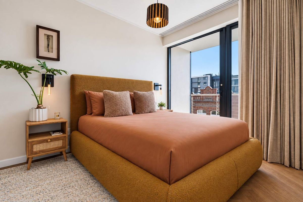 A well-maintained bedroom featuring hardwood flooring, modern wall-mounted lighting, and a large sliding glass door providing access to a private balcony.