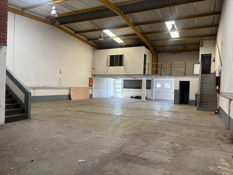 Spacious industrial warehouse unit featuring a mezzanine level, concrete flooring, exposed steel roof trusses, and dual staircases for versatile operational use.