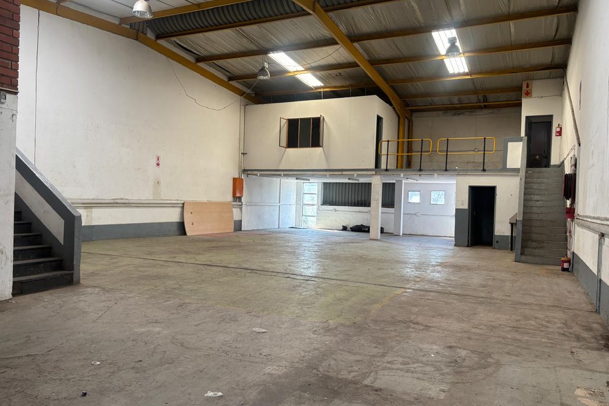 Spacious industrial warehouse unit featuring a mezzanine level, concrete flooring, exposed steel roof trusses, and dual staircases for versatile operational use.