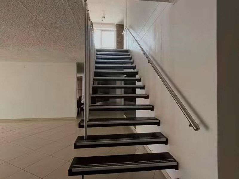 A bright, open hallway featuring a modern floating-style staircase with stainless steel handrails and neutral tiled flooring.