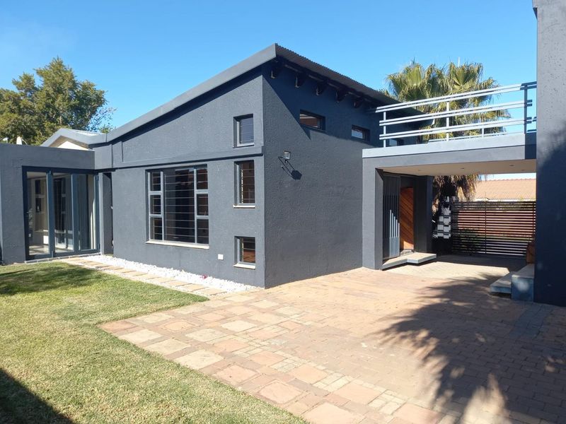 Modern rear exterior view featuring a dark-painted facade, paved patio area, elevated balcony with metal railings, and well-maintained lawn.