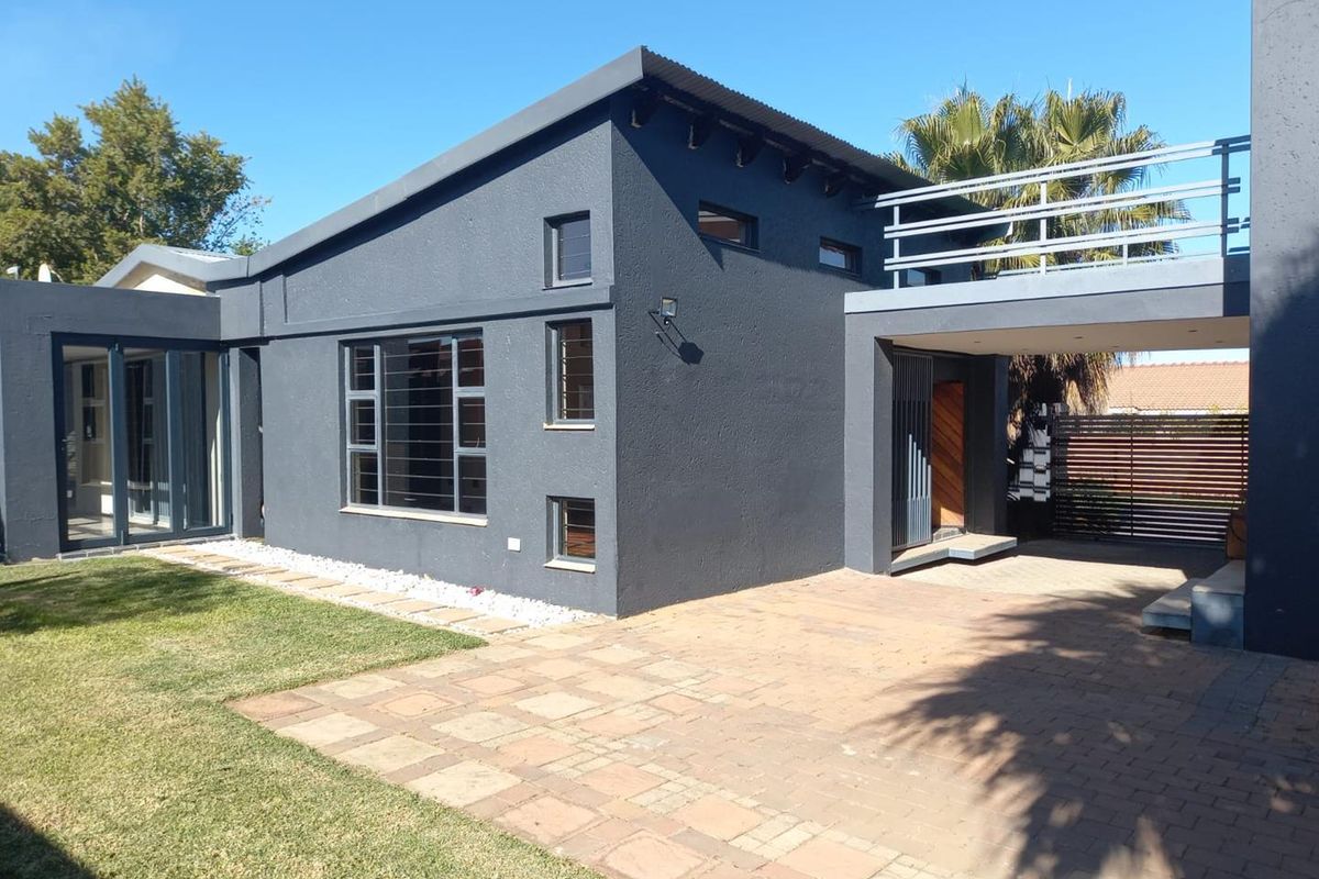 Modern rear exterior view featuring a dark-painted facade, paved patio area, elevated balcony with metal railings, and well-maintained lawn.