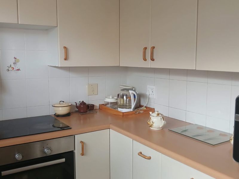 A functional kitchen featuring light-toned cabinetry, laminate countertops, a ceramic tile backsplash, and a built-in electric oven and hob.