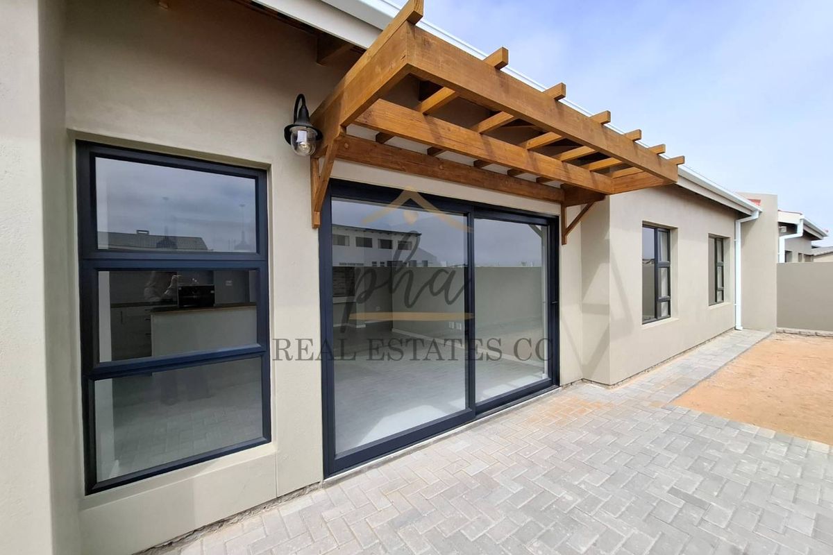 Rear exterior view of the townhouse featuring a paved patio area, timber pergola, and modern sliding glass doors leading into the living space.