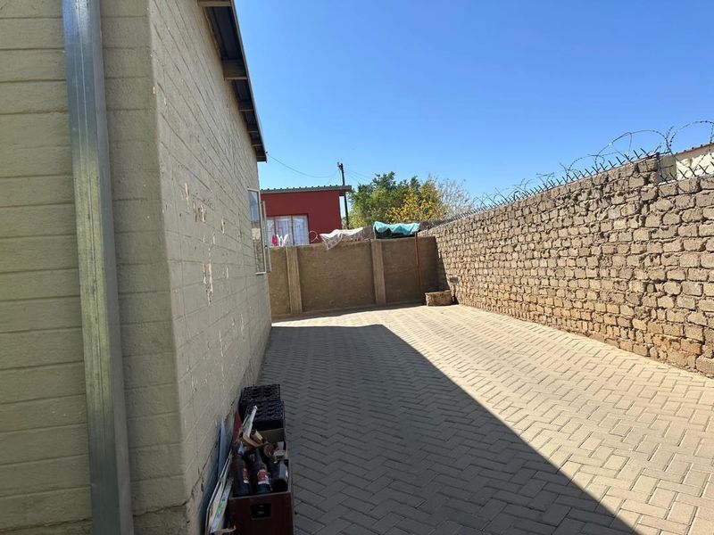 A rear exterior view showing a paved side yard, brick boundary wall with security razor wire, and the side elevation of the house.