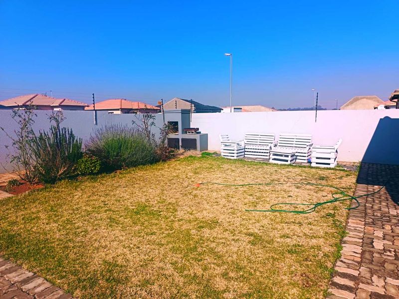 A private backyard featuring a built-in braai, perimeter wall with electric fencing, and a paved walkway bordering a lawn area.