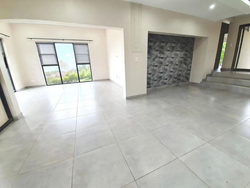 Spacious open-plan living area featuring large format floor tiles, a stone veneer feature wall, and large windows with natural light.