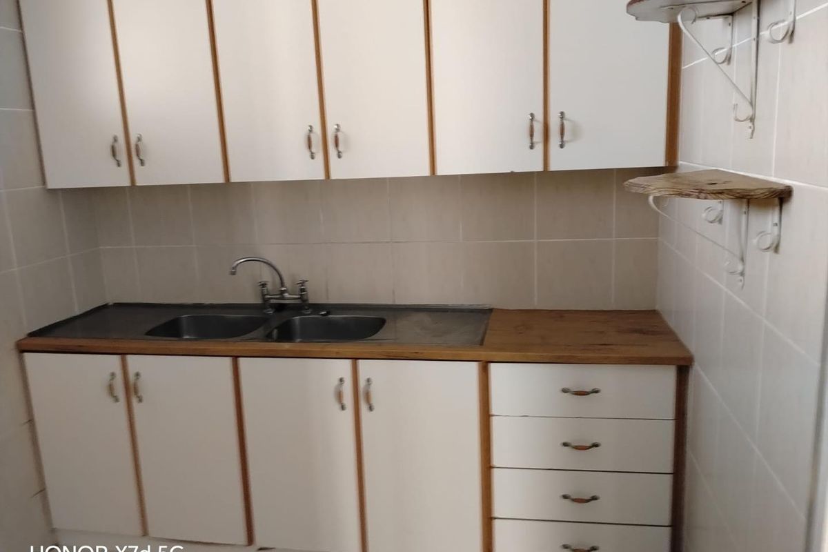 A functional kitchen area featuring white cabinetry, a double stainless steel sink, and tiled splashbacks, offering a clean and practical workspace.