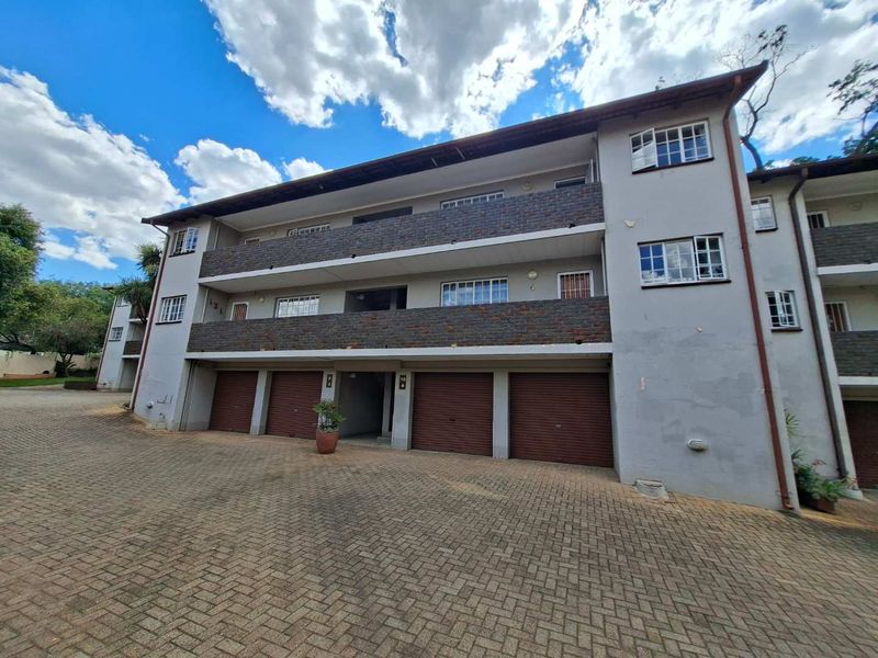 Exterior view of a multi-story apartment building featuring brick accents, private balconies, and ground-level garage access with a paved driveway.