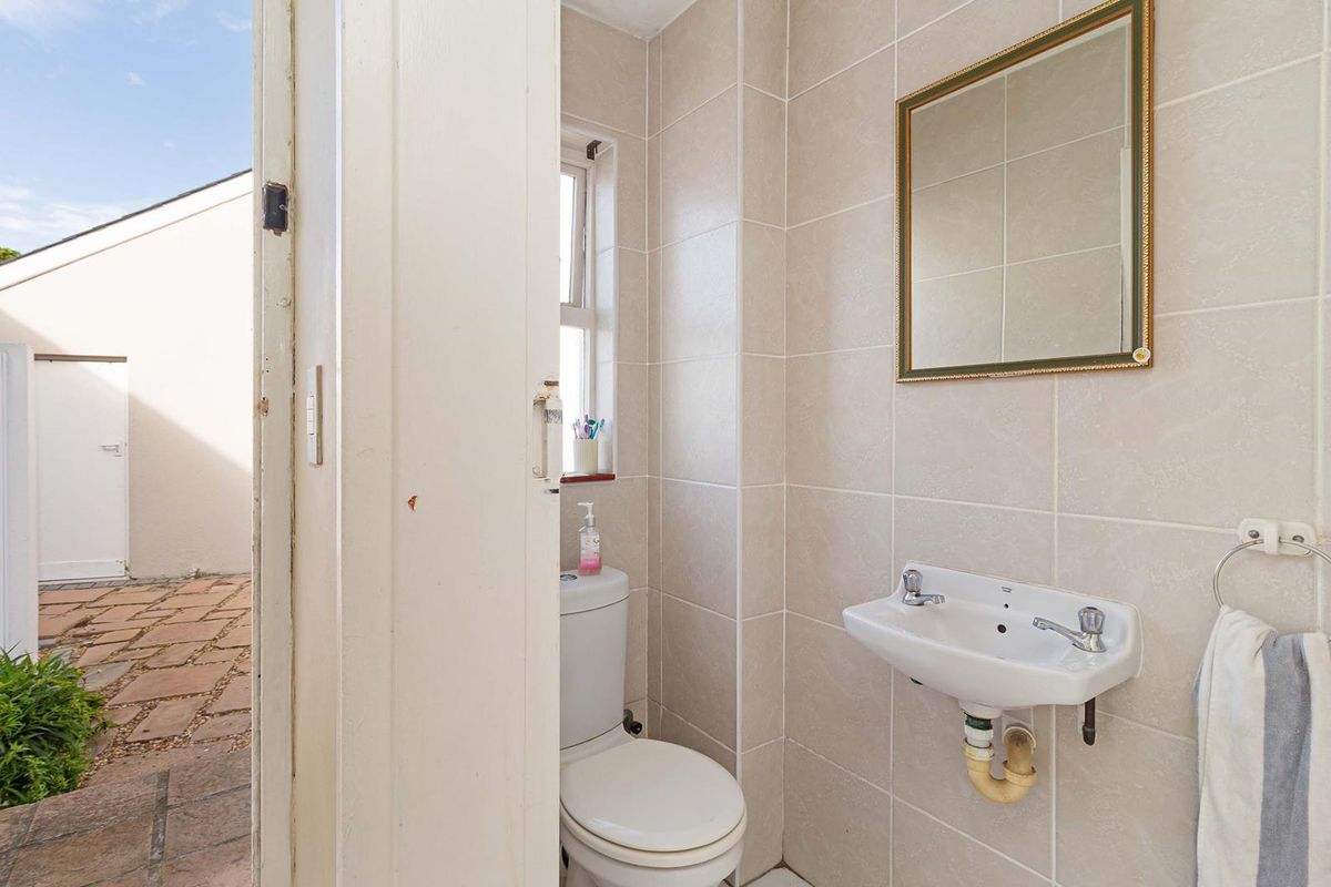 A compact bathroom featuring tiled walls, a wall-mounted basin, and a dual-flush toilet, with direct access to an outdoor patio area.