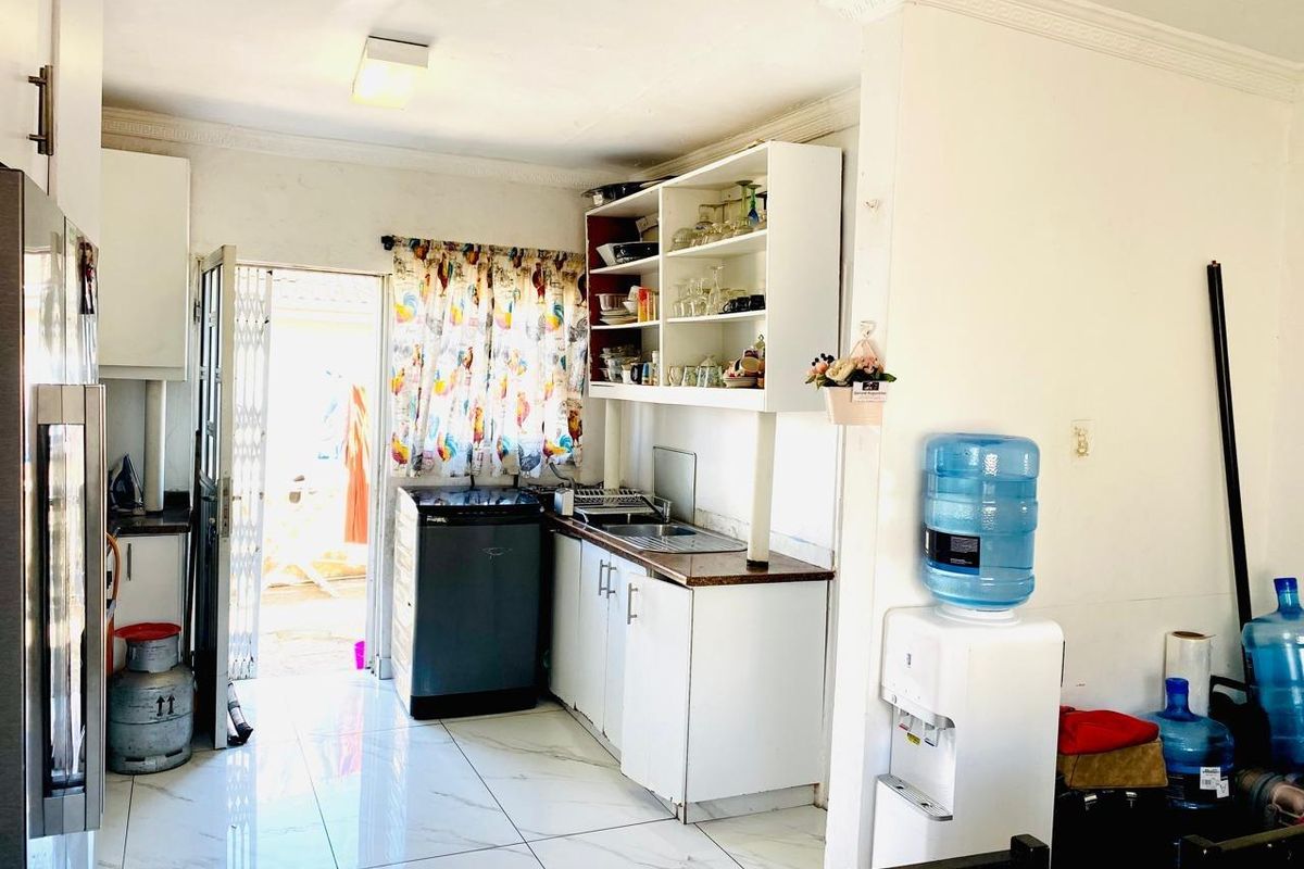 A functional kitchen area featuring built-in cabinetry, a stainless steel sink, and tiled flooring with direct access to an outdoor space.
