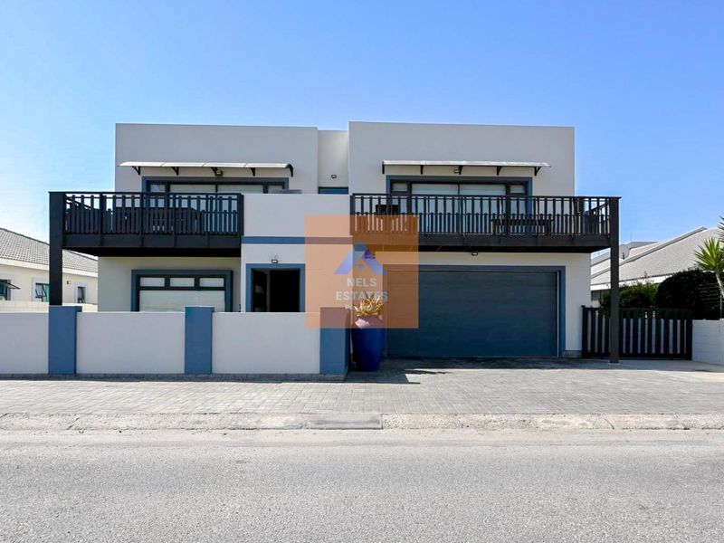 Modern double-story residential property featuring a paved driveway, double garage, and an upper-level balcony with dark metal railings.